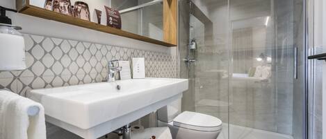 Un baño moderno con ducha de vidrio, lavamanos blanco y un inodoro.