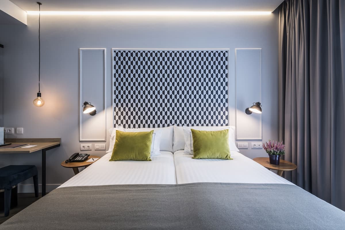 A modern hotel room with a large bed, two bedside tables, a desk, and a chair.