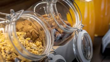 Una barra de desayuno con frascos de vidrio que contienen granola y otros productos para el desayuno, y una botella de jugo de naranja al fondo.