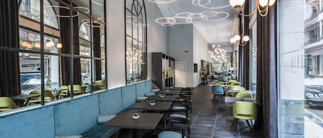 A modern restaurant with high ceilings, large windows, and a row of tables and chairs.
