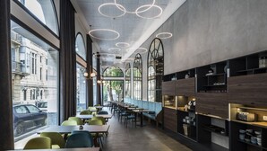 En moderne café med store vinduer, runde hængende lamper og træhylder med køkkenartikler.