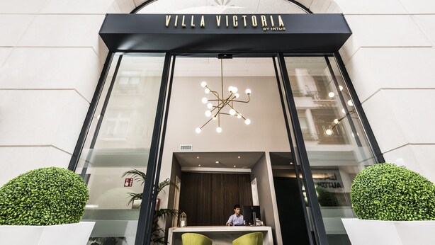 Indgangen til Villa Victoria af Intur, med et moderne design, en glasfacade, en indbydende reception og en markant lysekrone.