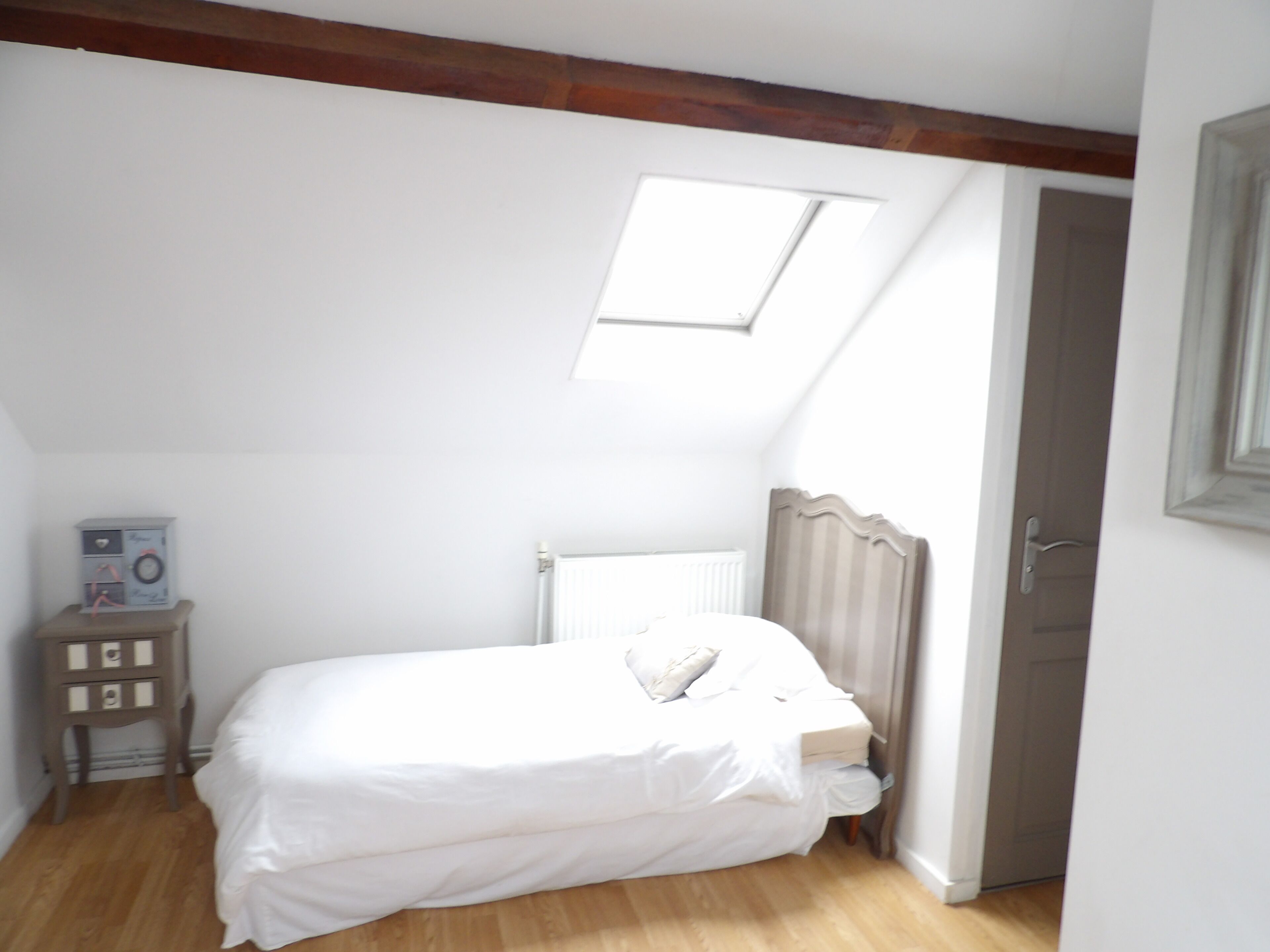 A bedroom with a skylight, a radiator, a wooden floor, and a small cabinet with drawers.