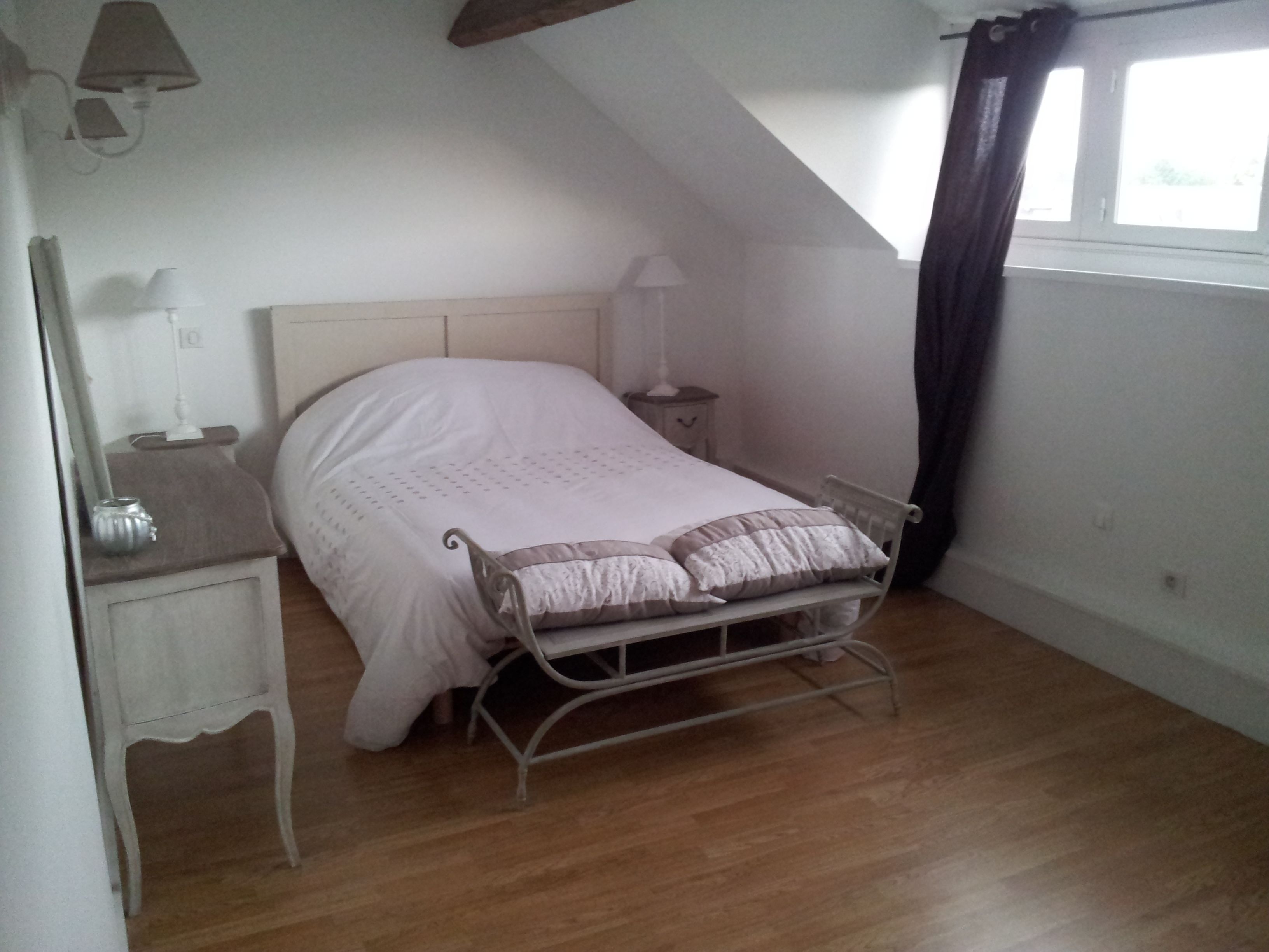Quarto com uma cama de solteiro, mesa de cabeceira, luminária e janela com cortinas.