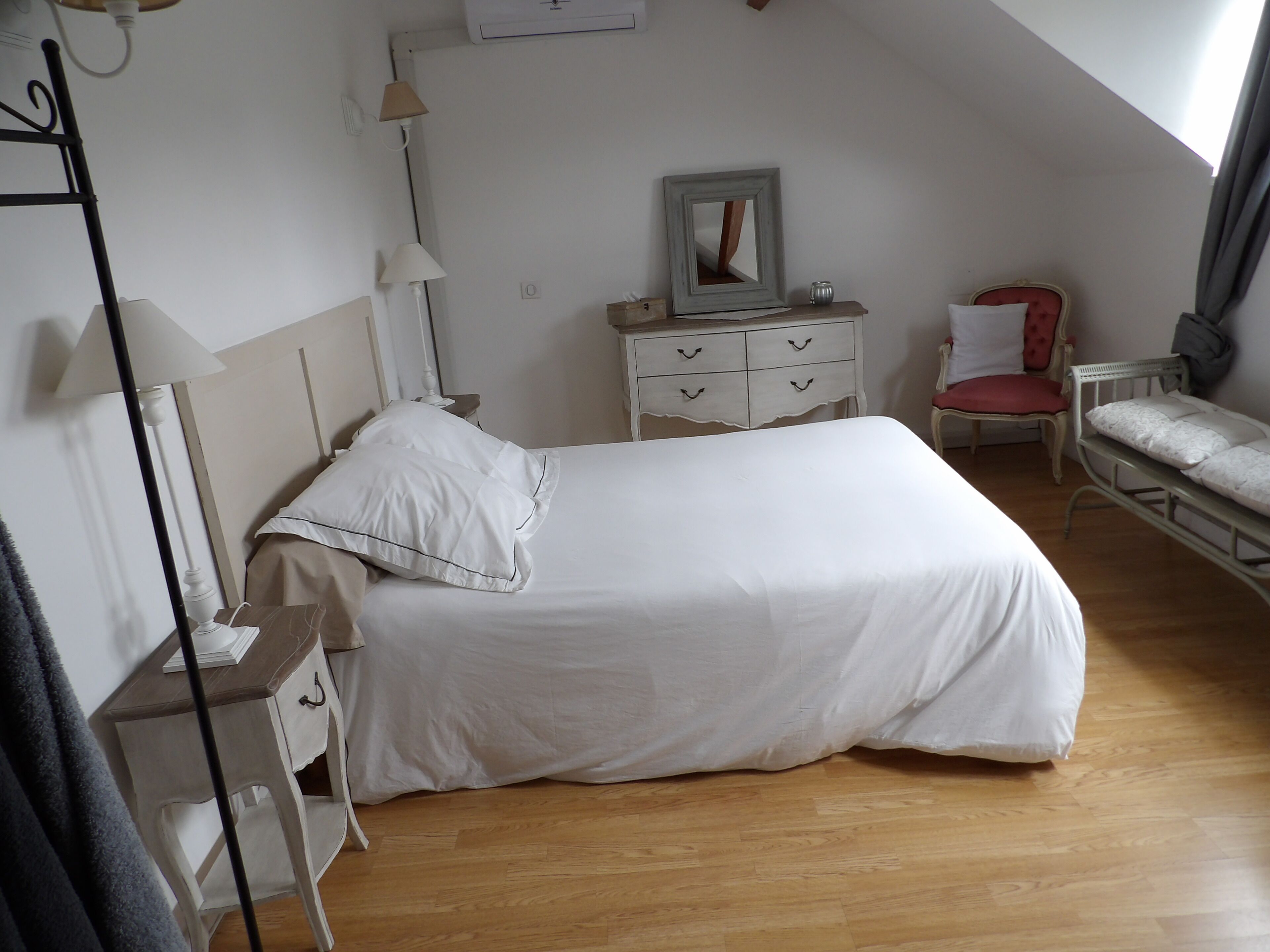 Une chambre à coucher bien rangée, avec un lit, des tables de chevet, une chaise et une petite table sur laquelle se trouve une lampe.