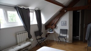 A bedroom with a bed, two chairs, a radiator, a desk with a bottle, and a painting on the wall. - Le Clos Verlaine (Fampoux)