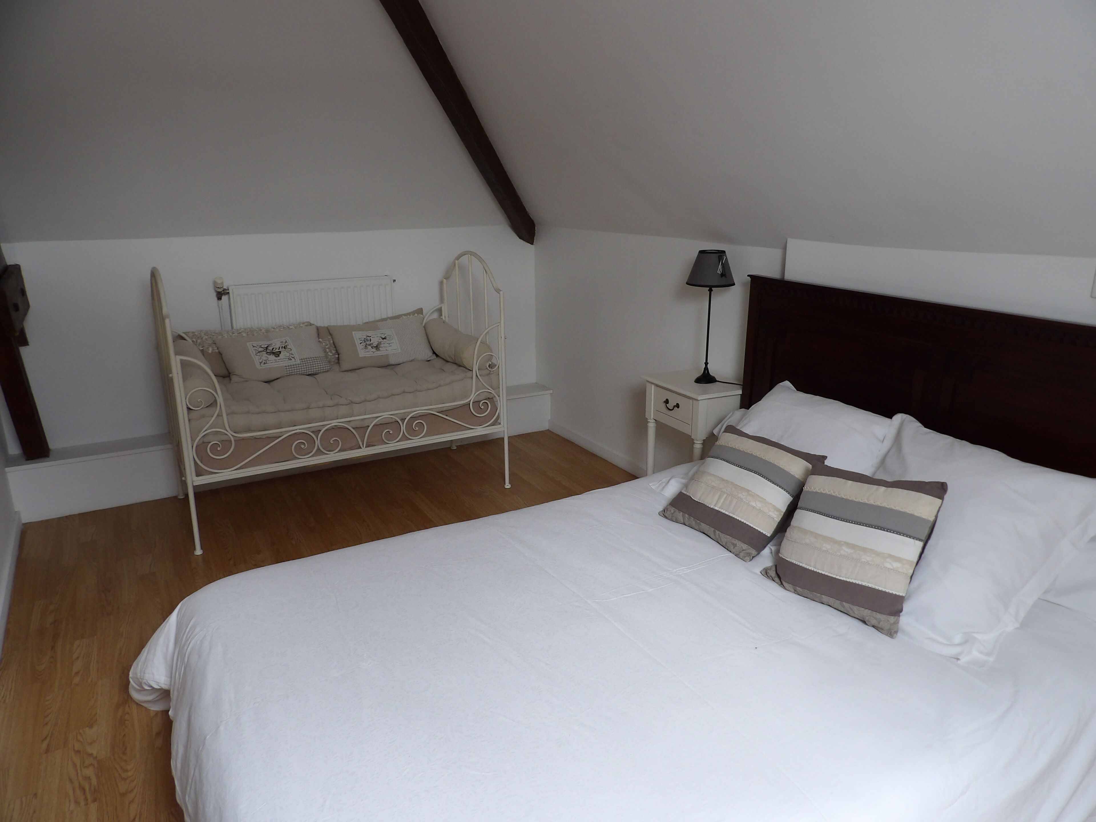 Un dormitorio con cama, una banqueta, una mesita de noche con lámpara y suelo de madera.