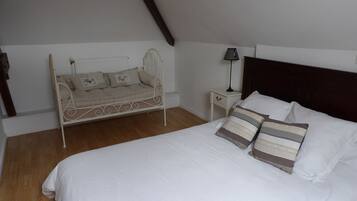 Un dormitorio con cama, una banqueta, una mesita de noche con lámpara y suelo de madera.
