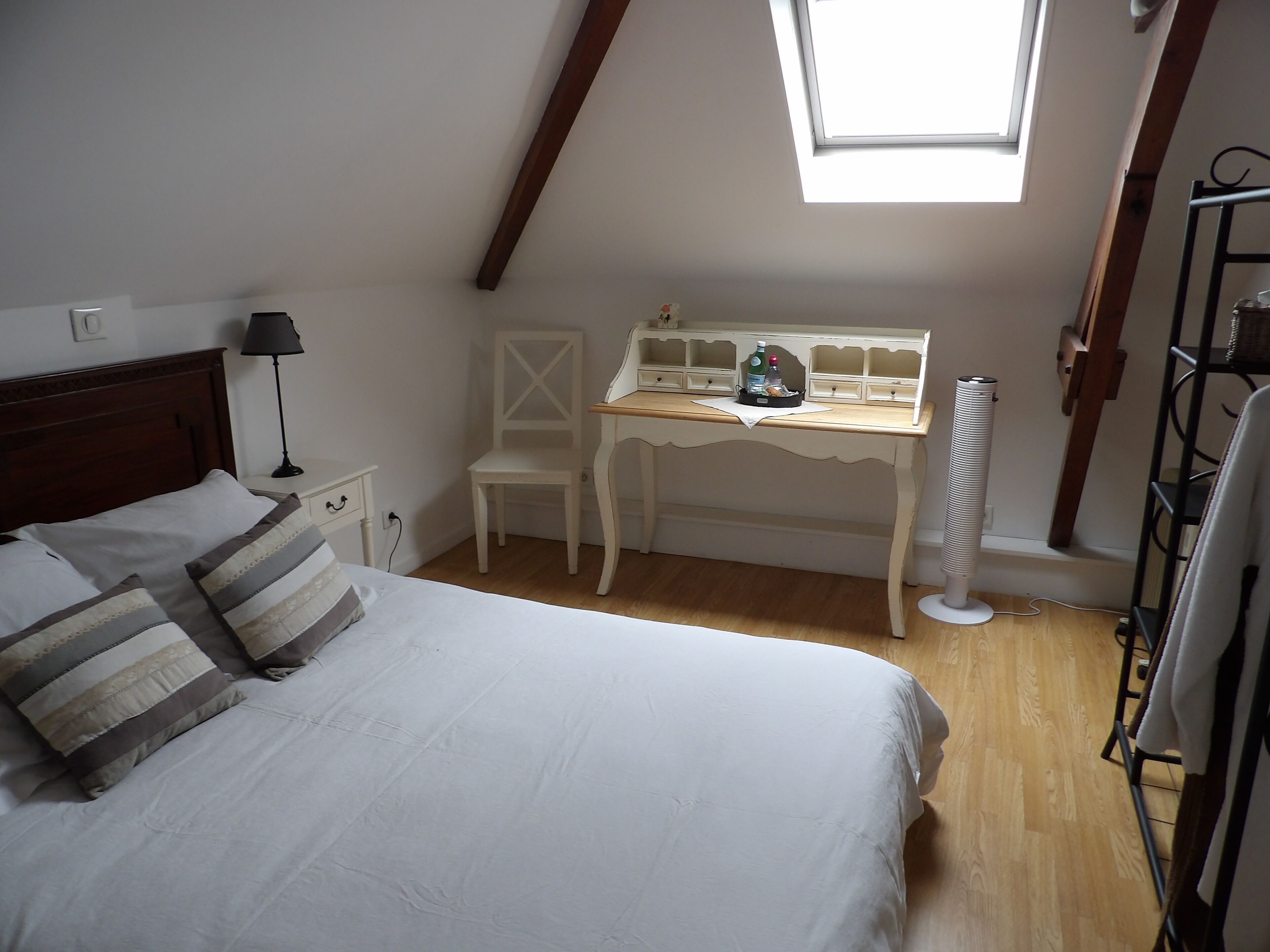 A bedroom with a bed, a desk, a chair, and a skylight.