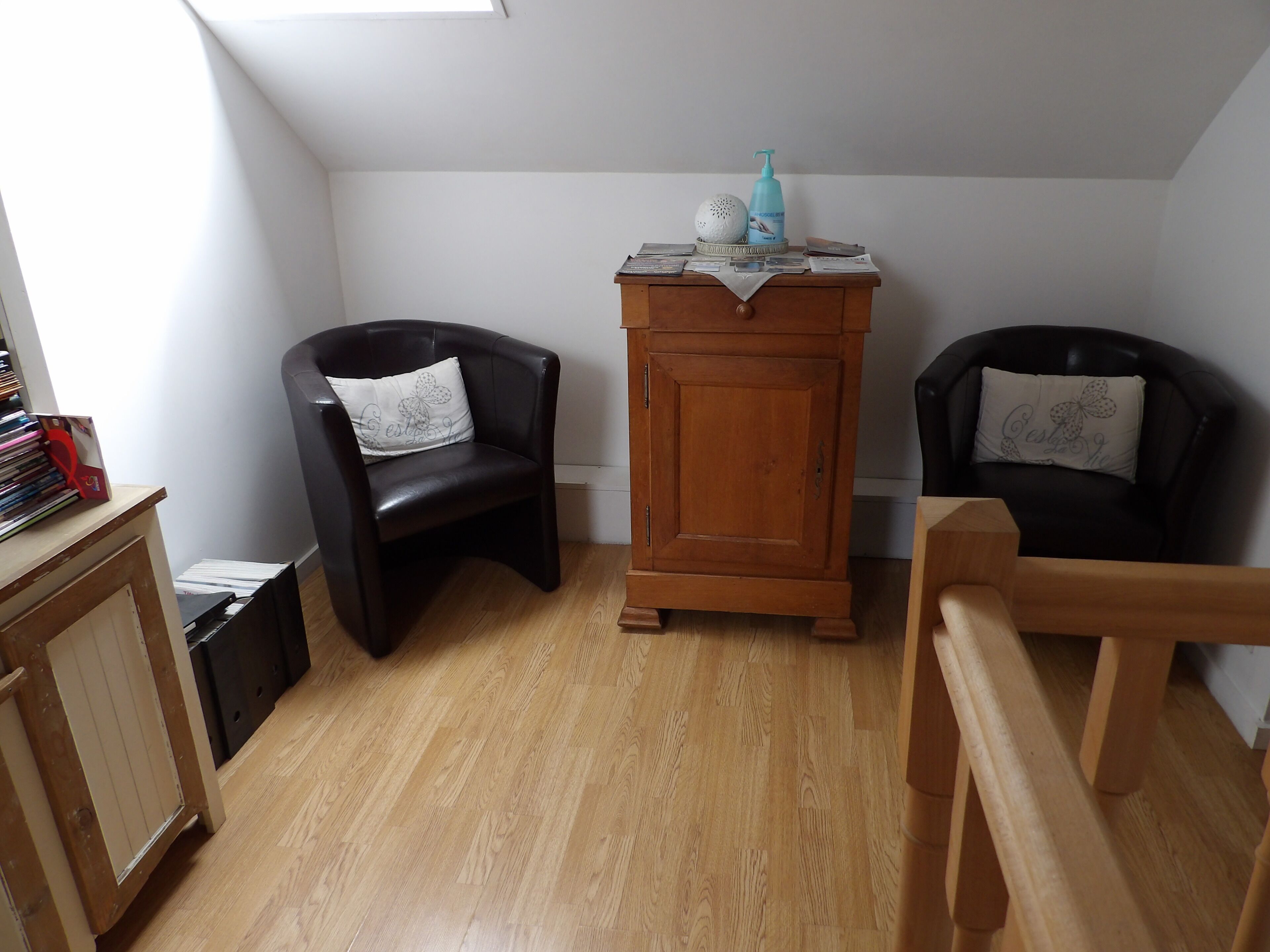 A room with two black leather chairs, a wooden cabinet, and a small table with a blue bottle and decorative items.