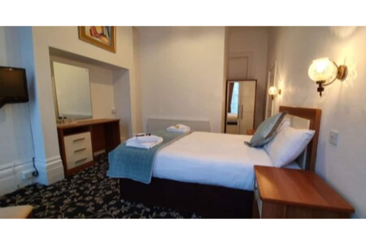 A hotel room with a bed, bedside tables, a desk, a chair, a TV, and a mirror.
