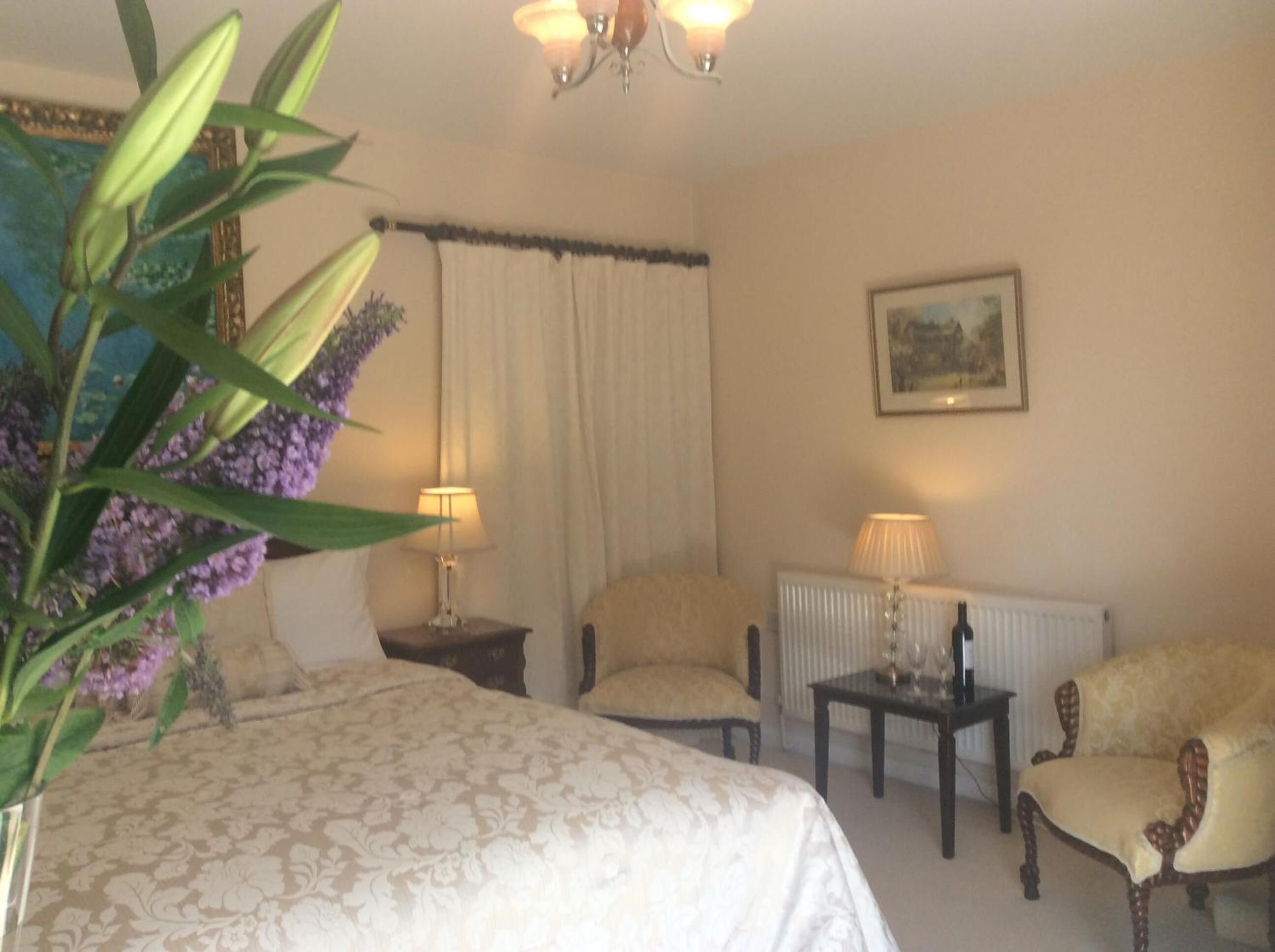 A hotel room with a bed, two chairs, a table, a radiator, and a lamp.