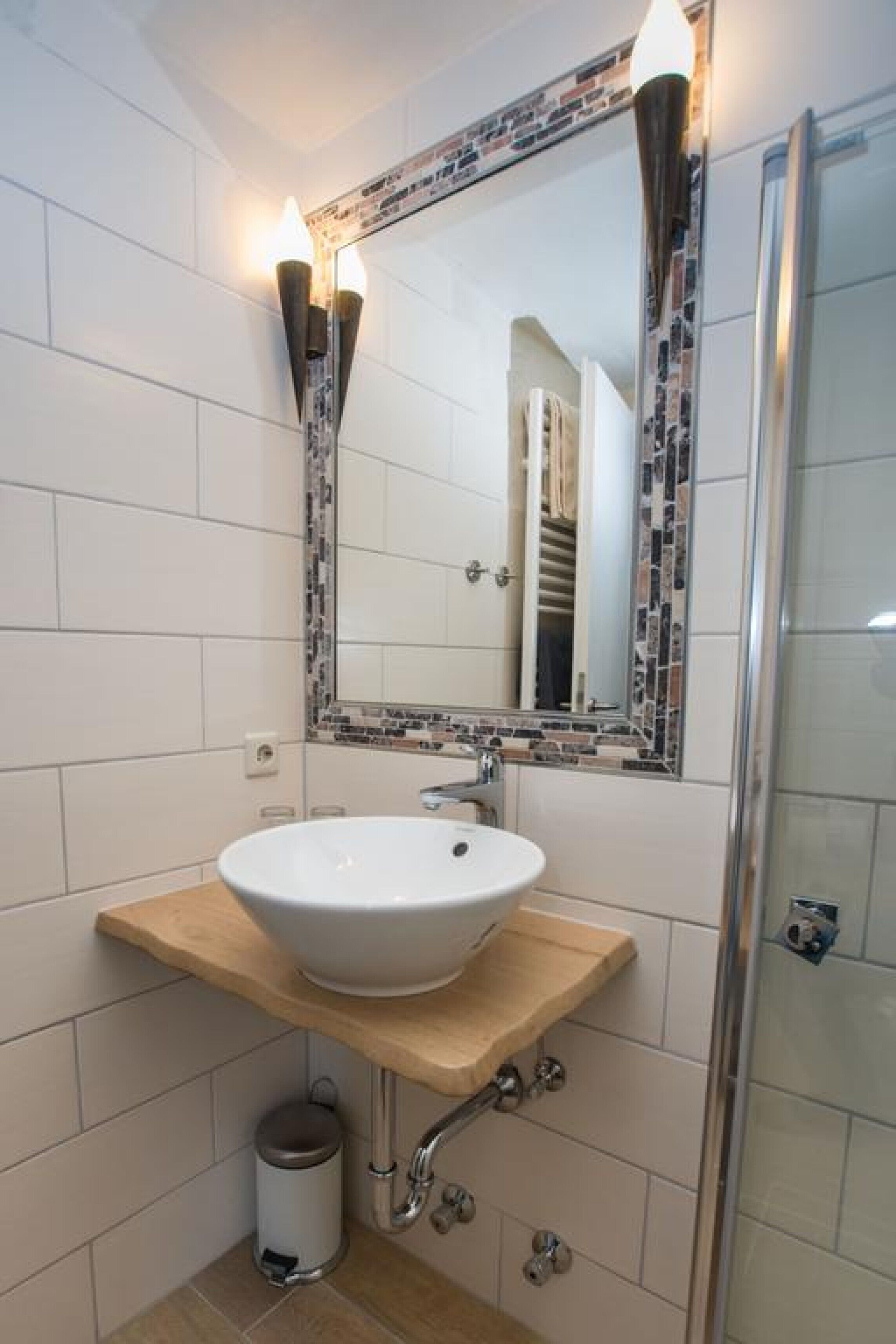 A bathroom with a white sink, a mirror with a mosaic frame, and a shower area.