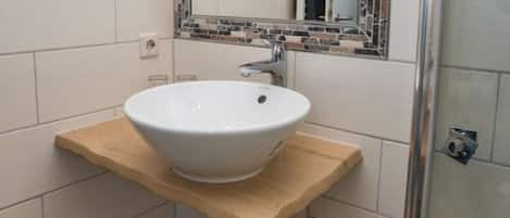 A bathroom with a white sink, a mirror with a mosaic frame, and a shower area.