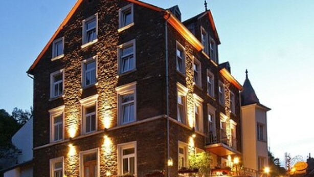 Ein mehrstöckiges Hotel mit einer Steinfassade, zahlreichen Fenstern und einem Restaurant im Erdgeschoss.