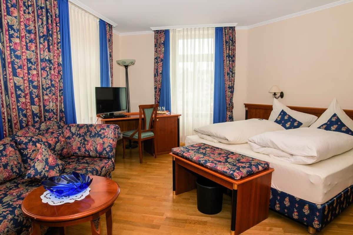 A hotel room with a bed, a sofa, a desk with a television, and a lamp.