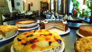 Eine Auswahl an Kuchen wird in einem Café präsentiert, im Hintergrund sind Tische und Stühle zu sehen.