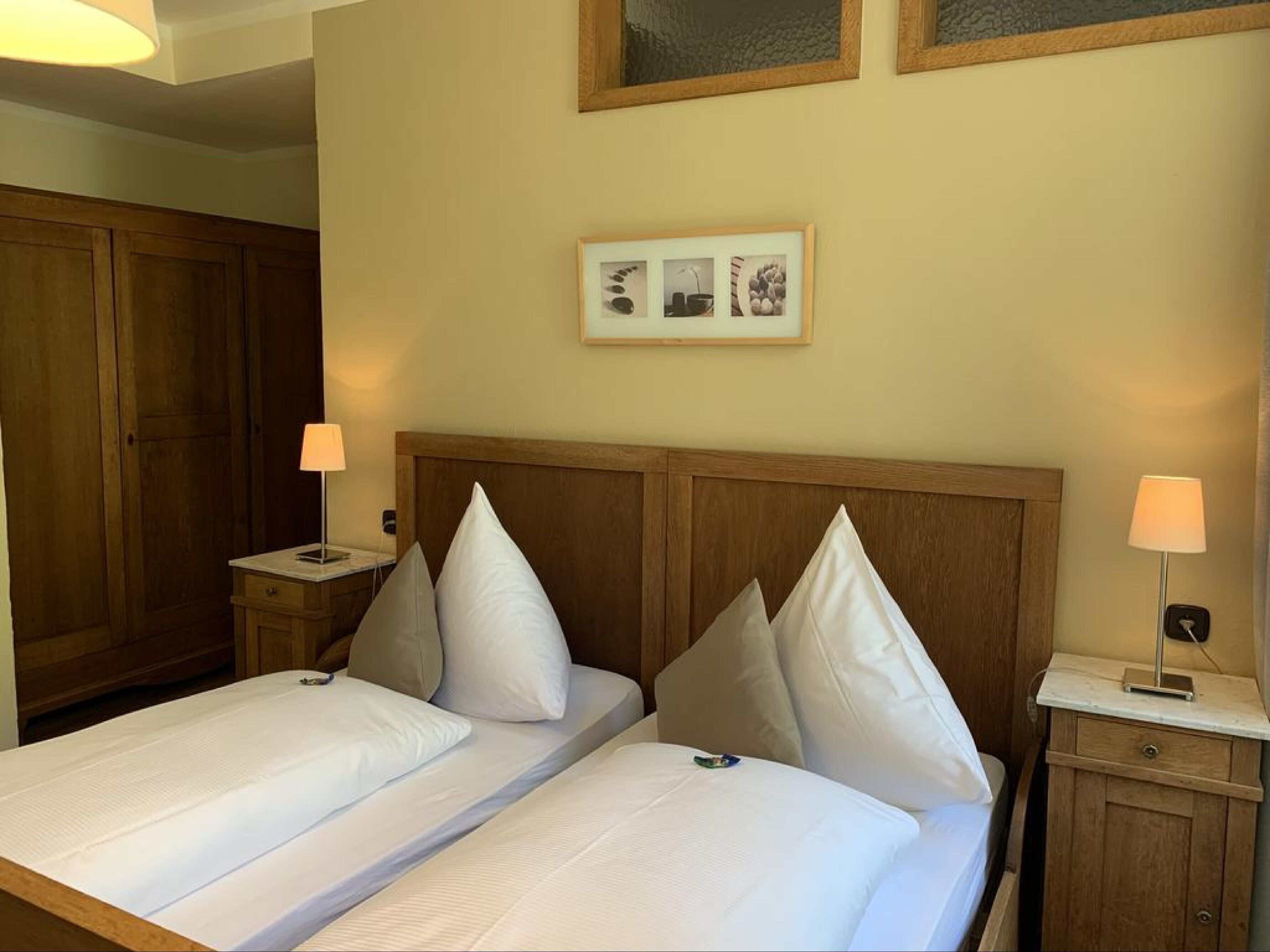 A hotel room with two beds, wooden headboards, a nightstand with a lamp, and a framed picture on the wall.