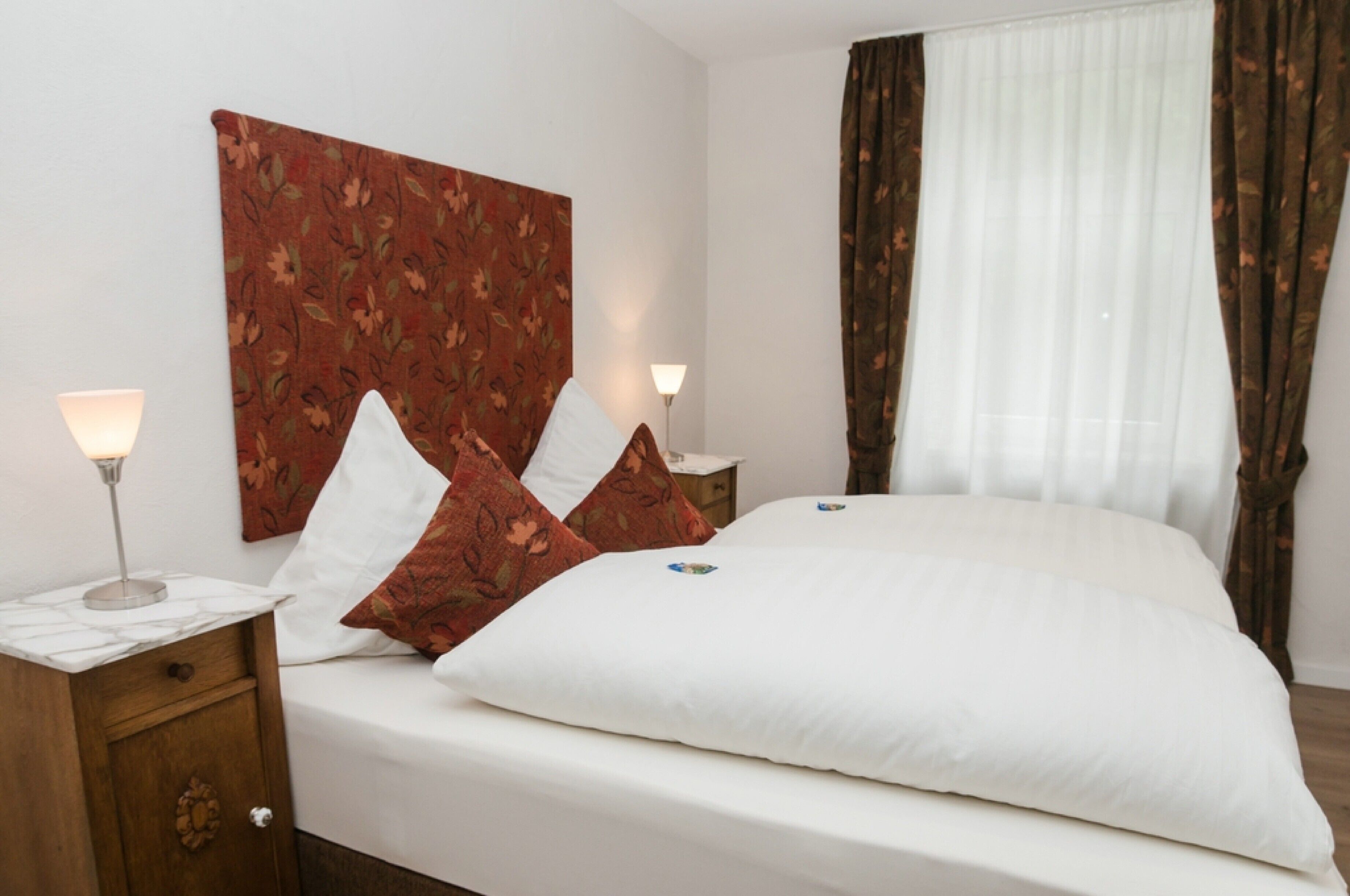 Ein Hotelzimmer mit einem großen Bett, zwei Nachttischen und einem Fenster mit Vorhängen.