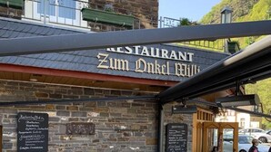 Ein Sitzbereich im Freien mit Tischen und Stühlen, eine Steinmauer und ein Schild für 'RESTAURANT Zum Dinkel Wild'.