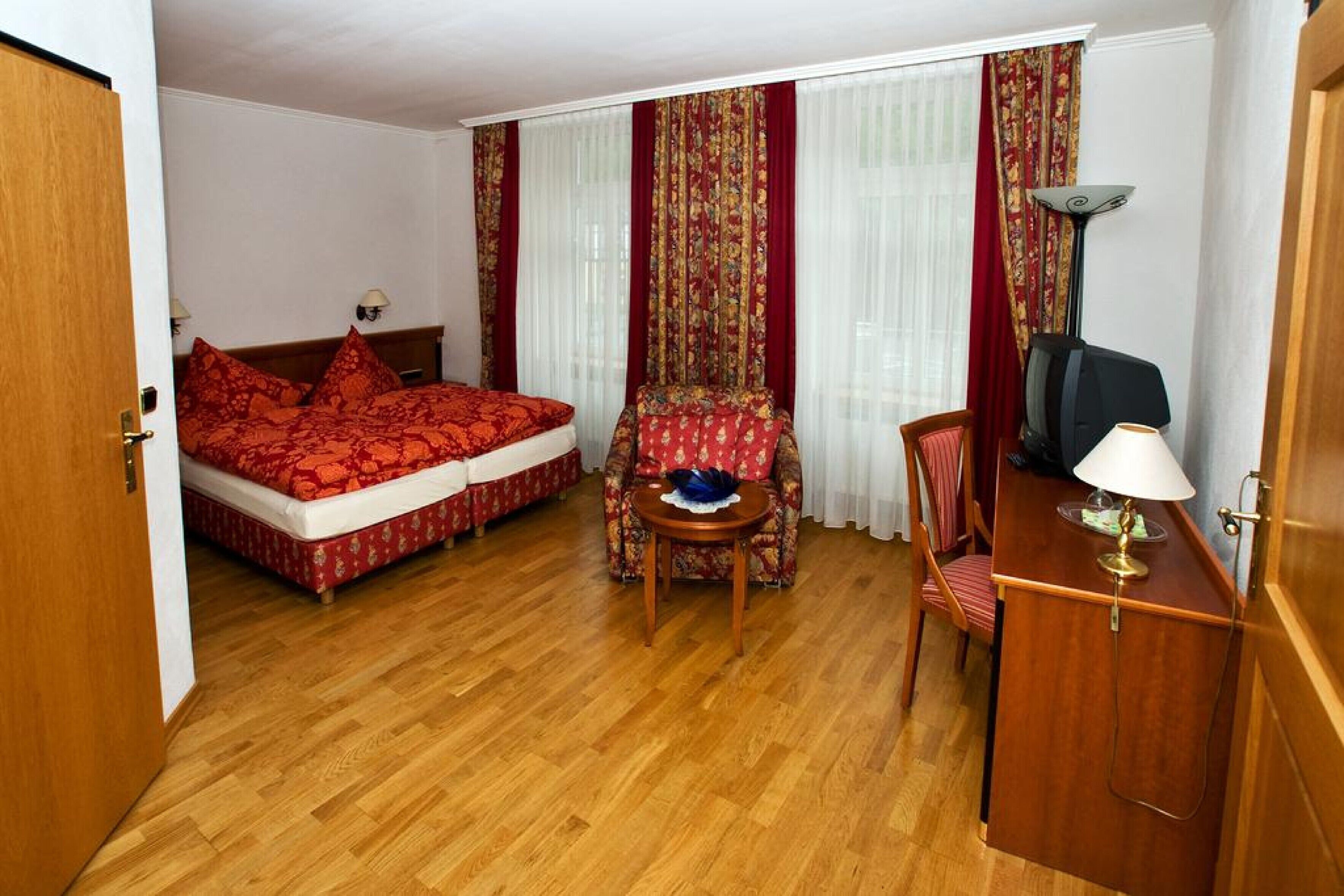 A hotel room with a bed, a chair, a desk, and a lamp.