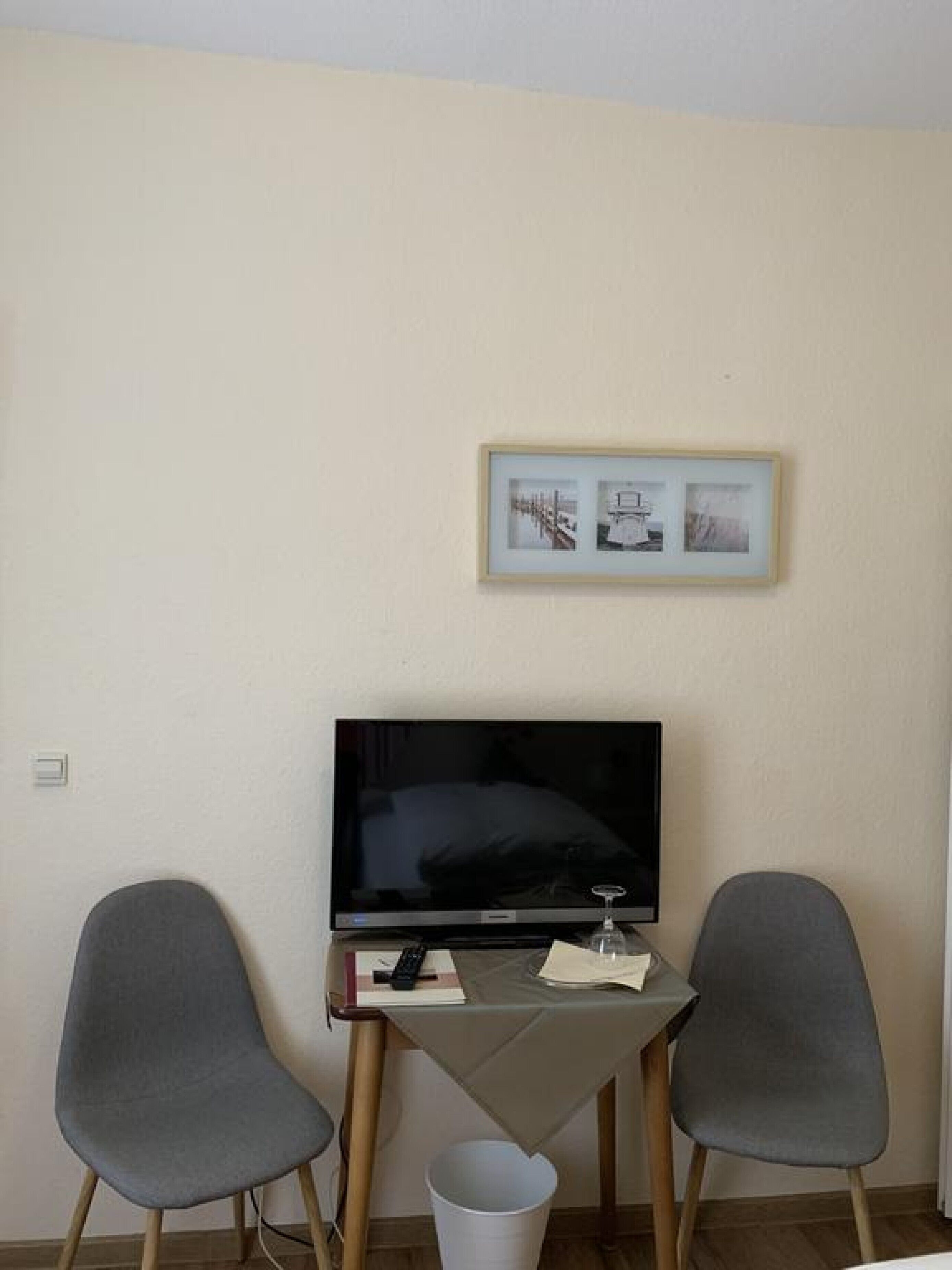 A small room with a television, two grey chairs, a small table, and a framed picture on the wall.