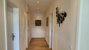 Ein Flur mit Holzboden, weißen Wänden und einem dekorativen Metallkunstwerk an der rechten Wand.