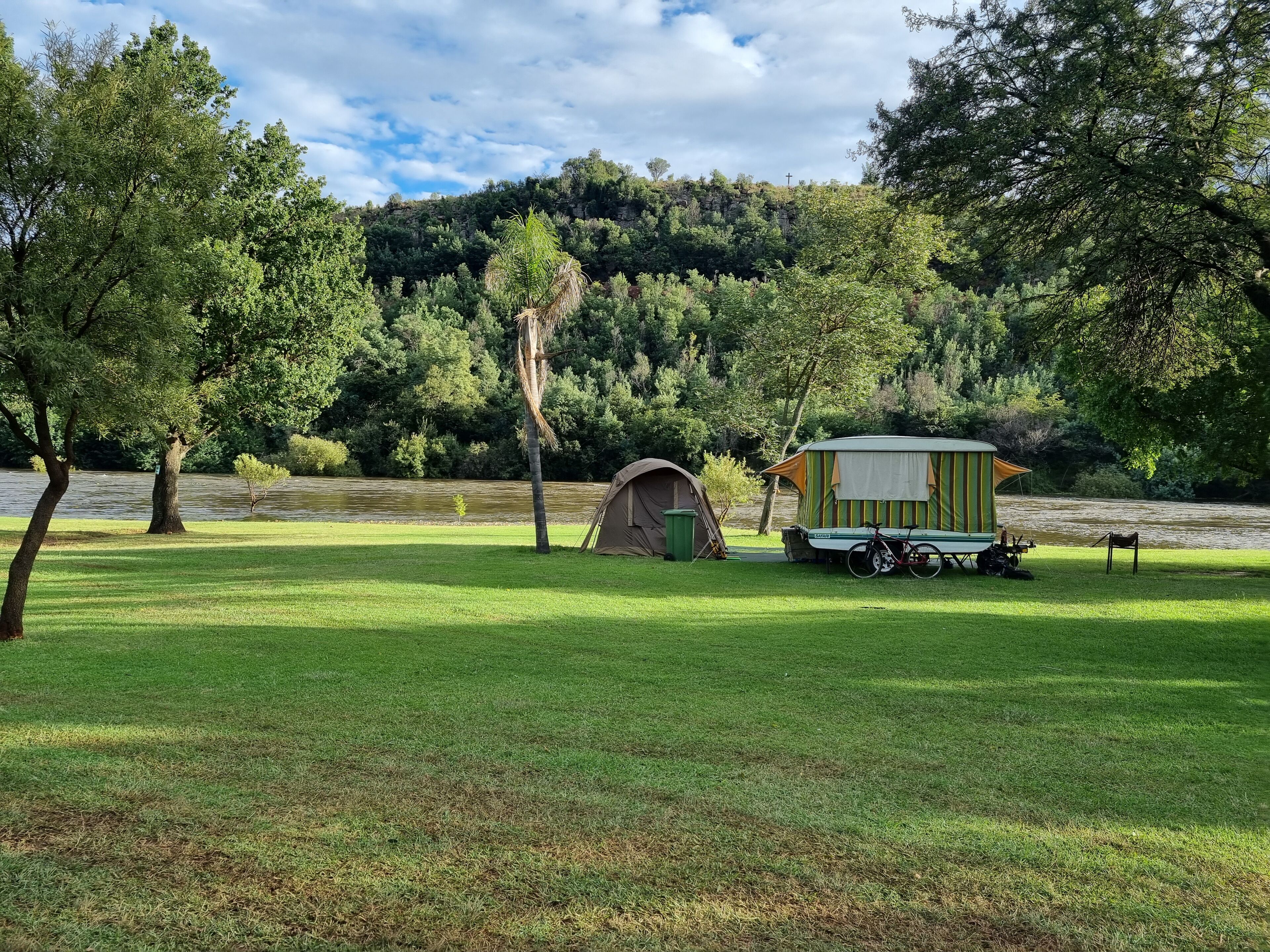 Un camping con una tienda de campaña y una pequeña cabaña junto a un lago, rodeado de árboles.