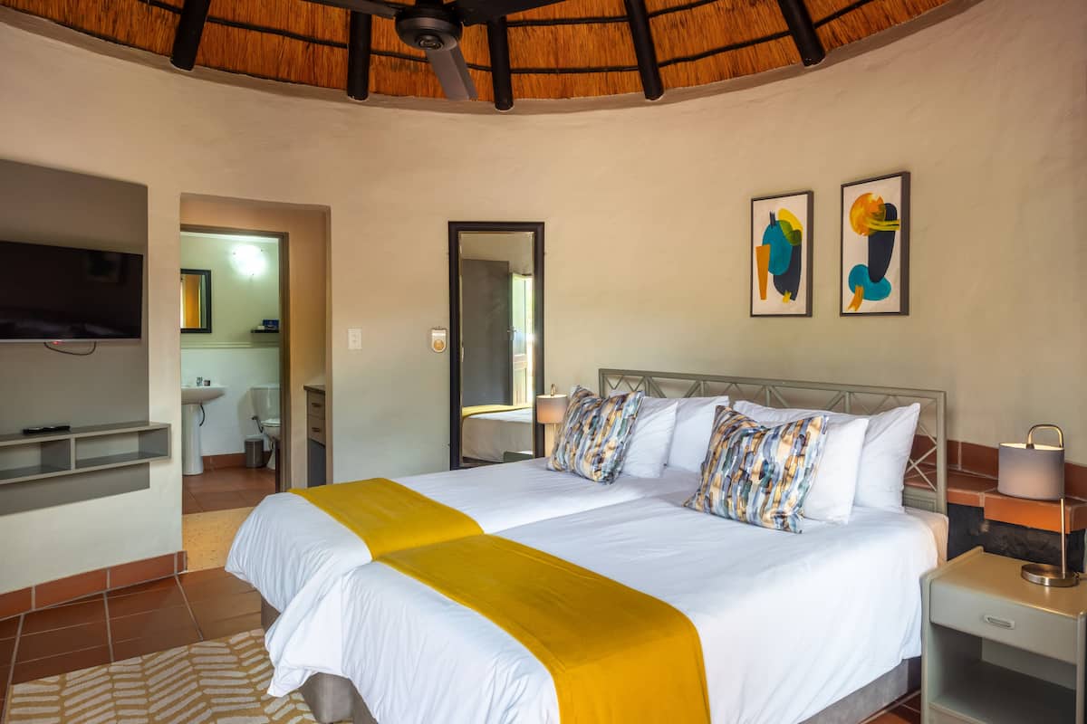 A hotel room with two beds, a TV, artwork on the wall, and a ceiling fan.