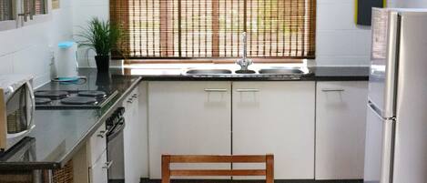 Une cuisine avec une table à manger dressée pour deux personnes, un panier de fruits et un réfrigérateur.