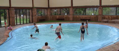 Una piscina interior con paredes de vidrio transparente, borde de ladrillo y estructura de techo.