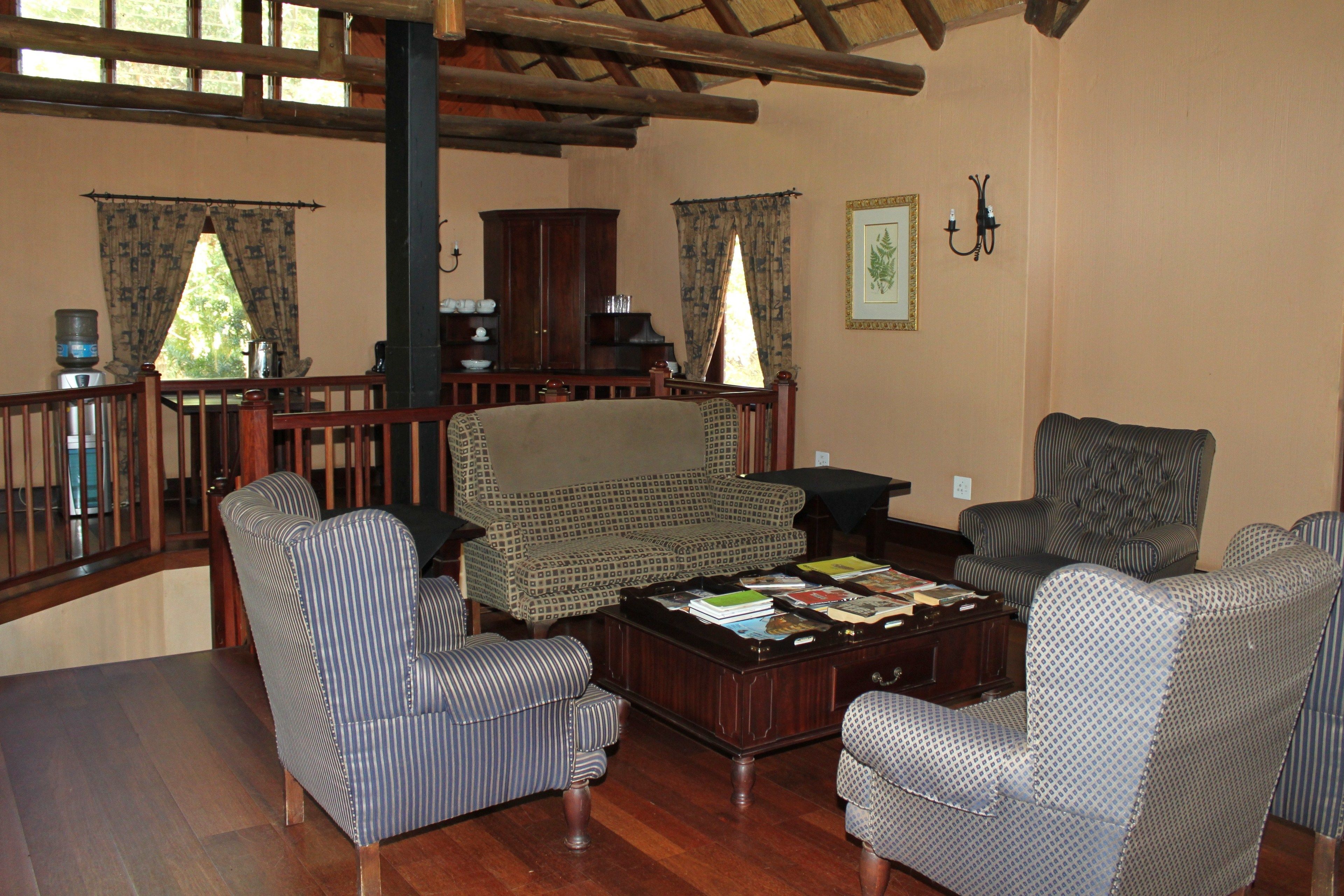 A spacious living room with a wooden staircase, a large armchair, a patterned sofa, and a coffee table with books and magazines.