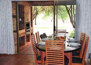 Un comedor con pared de ladrillo, puerta de cristal que da al exterior y una mesa lista para cuatro personas con sillas.
