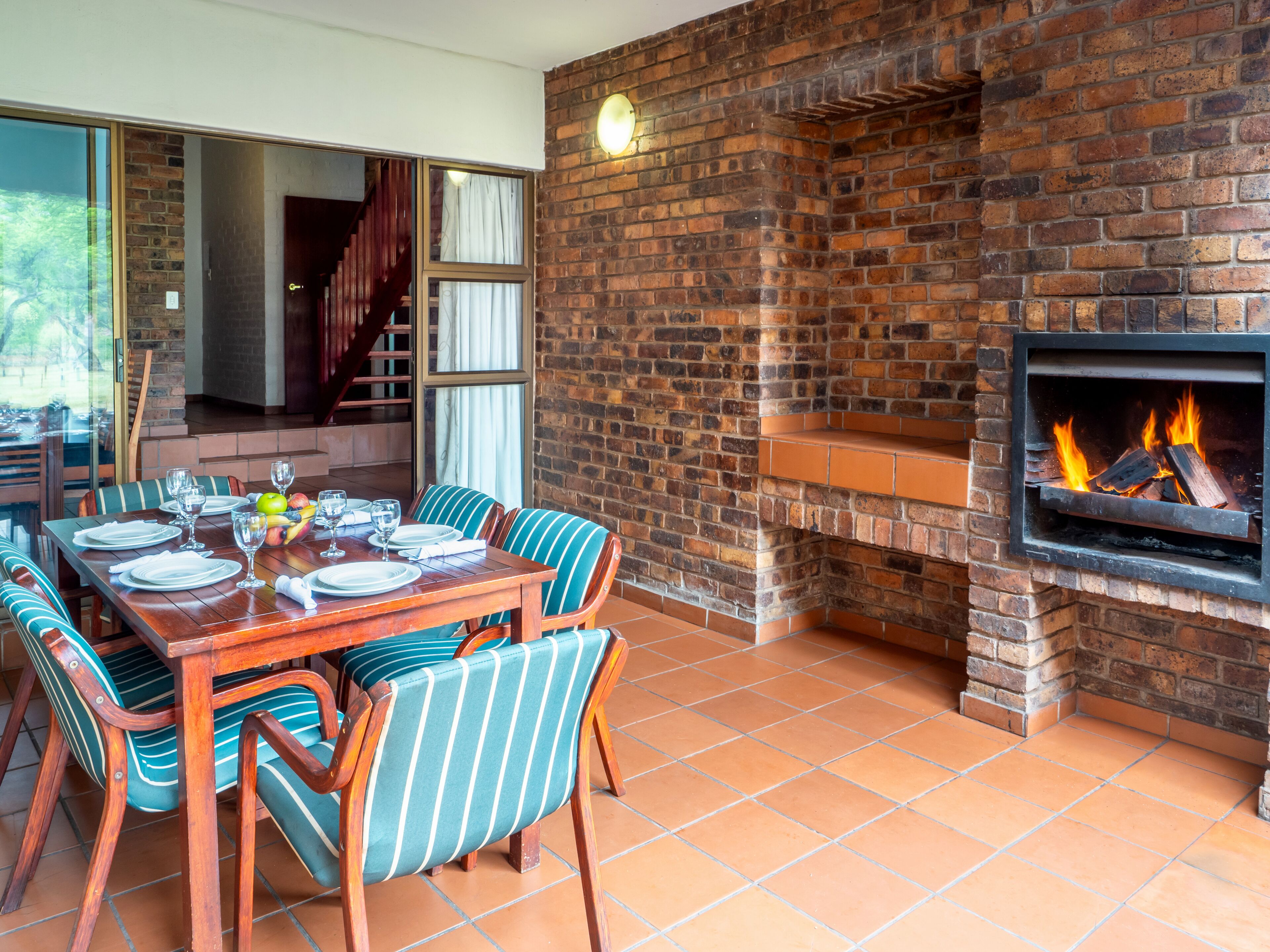 Un comedor con chimenea de ladrillo, una mesa de madera preparada para cuatro personas y sillas a rayas.