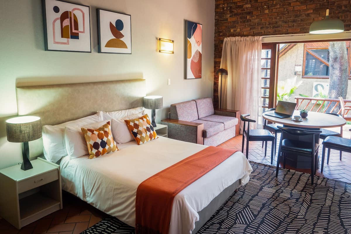 A hotel room with a bed, a sofa, a table with a laptop, and a view of the outdoors.
