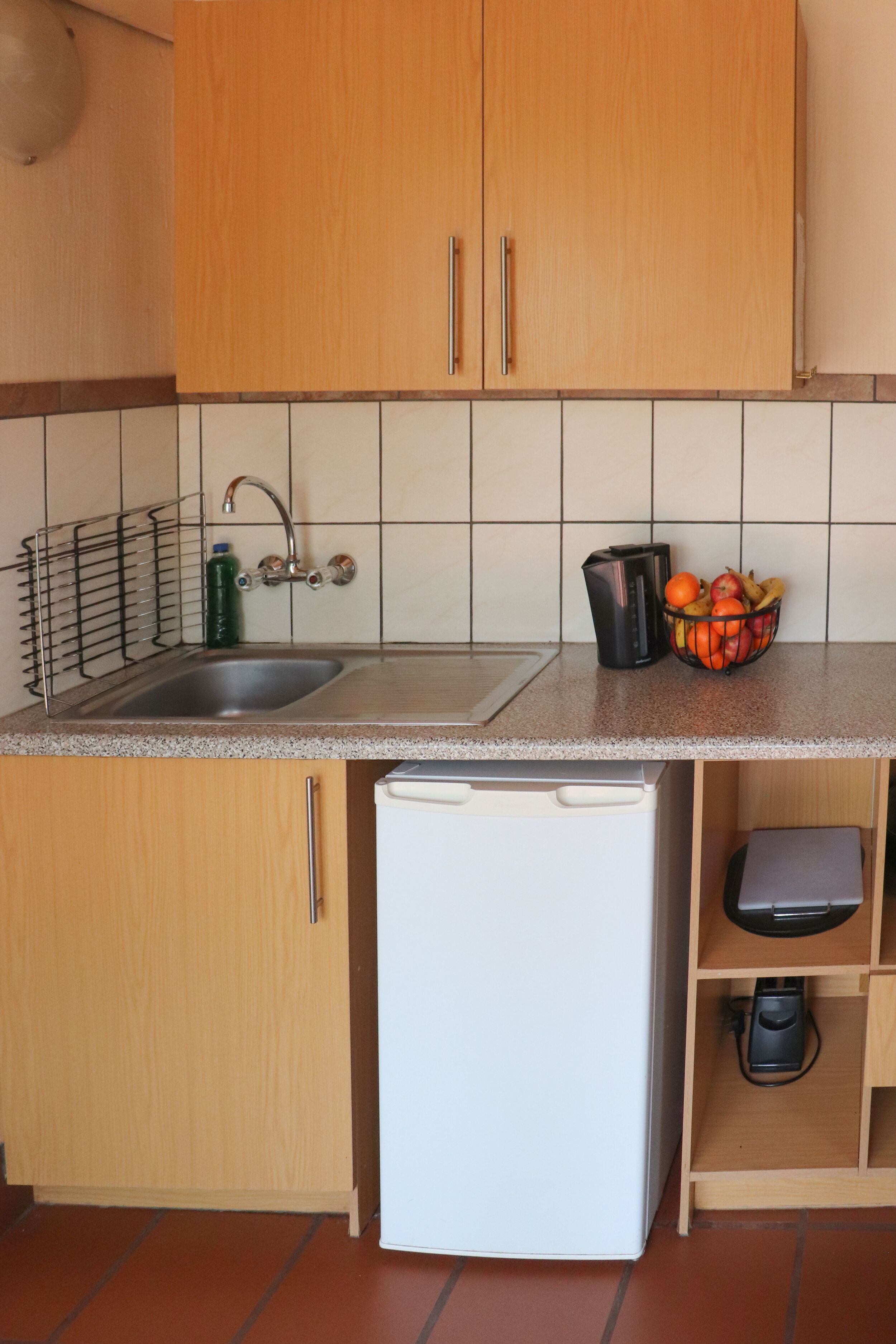 A kitchen with wooden cabinets, a stainless steel sink, a white refrigerator, a coffee maker, and a fruit basket on the countertop.