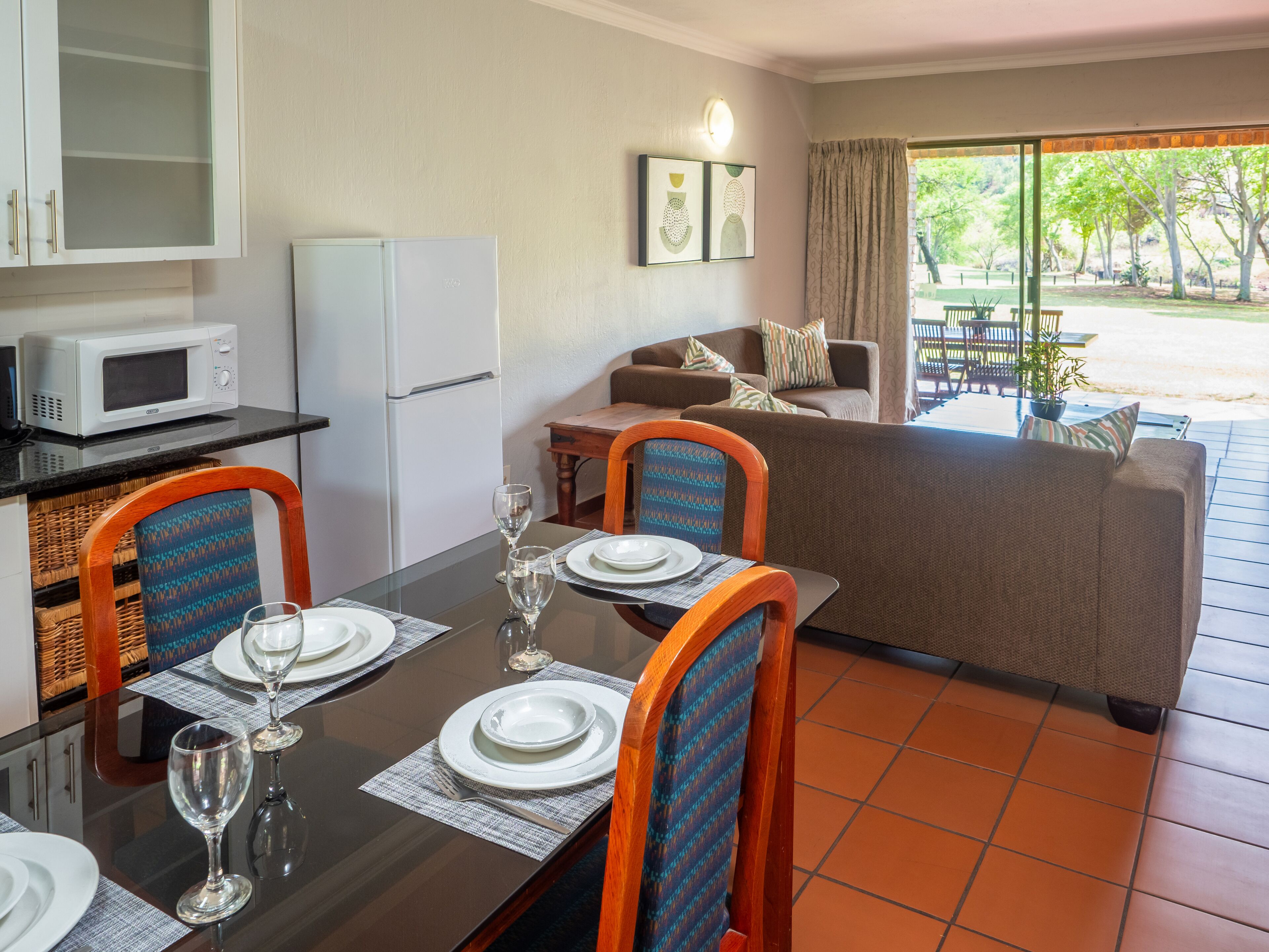 A dining area with a table set for four, a microwave, and a refrigerator in the background.