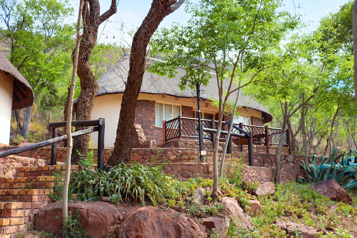 A rustic building with a thatched roof, surrounded by trees and rocks.