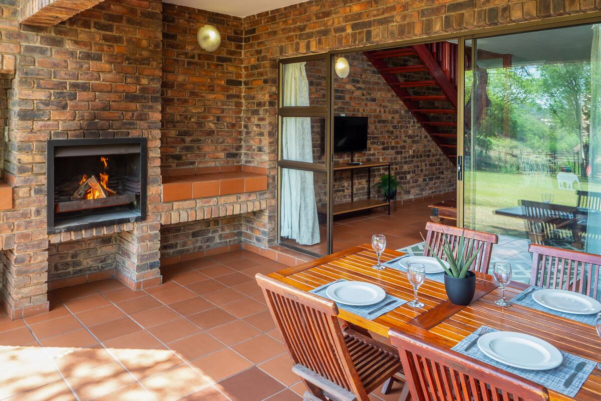A dining area with a brick fireplace, a TV, and a glass door leading to a garden.