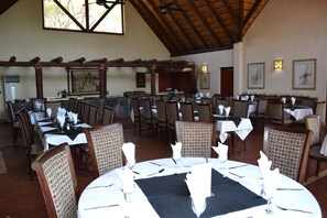 Un restaurante con varias mesas dispuestas para comer, que cuenta con un techo alto y vigas de madera.
