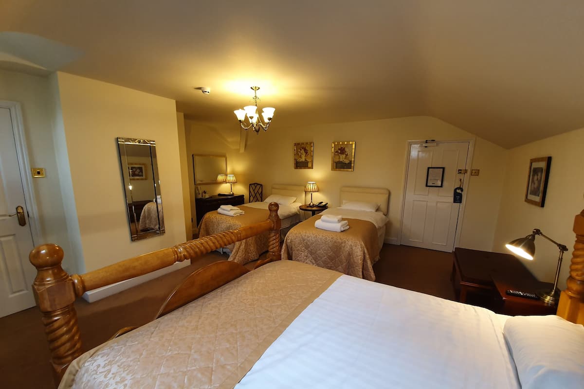 A hotel room with two beds, a chandelier, a mirror, and a desk with a lamp.