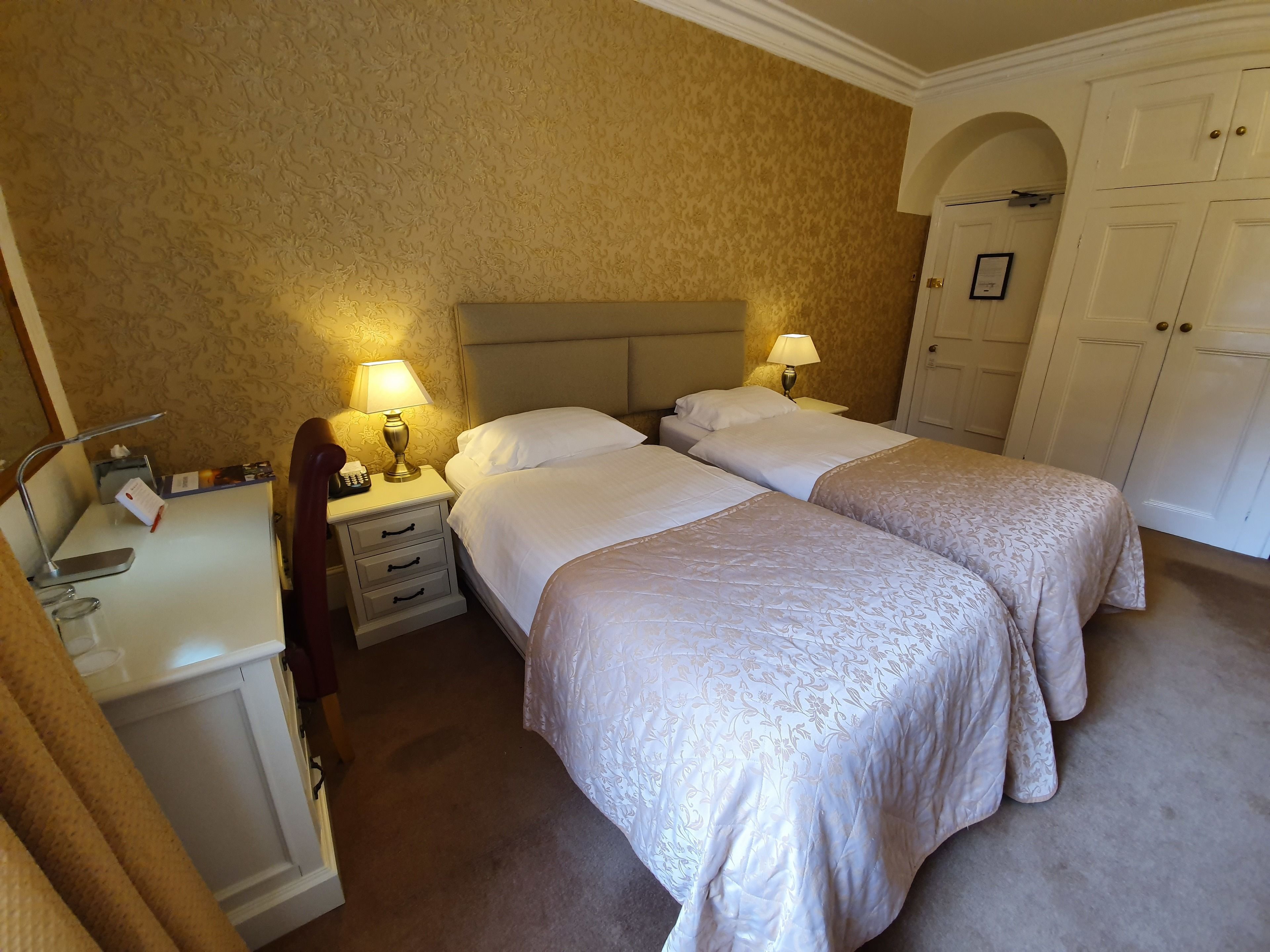 A hotel room with two beds, a desk, a chair, and a wardrobe.