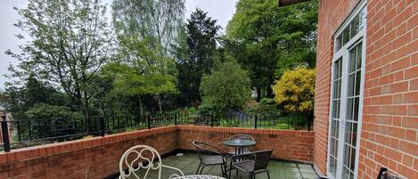 A patio with a round table and chairs, a brick wall, and a window.