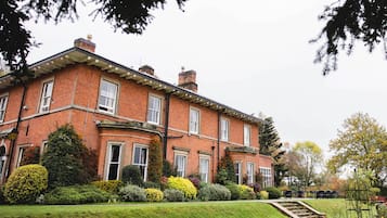 A large brick building with multiple windows, a well-maintained lawn, and a staircase leading to the entrance.