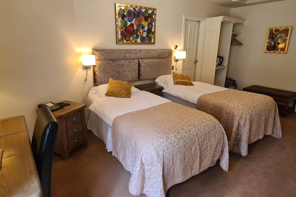 Une chambre d’hôtel avec deux lits, une table de chevet, une lampe, une chaise et un bureau avec une lampe.