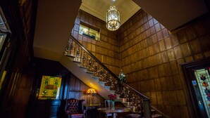 A grand staircase with a chandelier, a dining area with a table and chairs, and a carpeted floor. - The Upper House (Stoke-on-Trent)