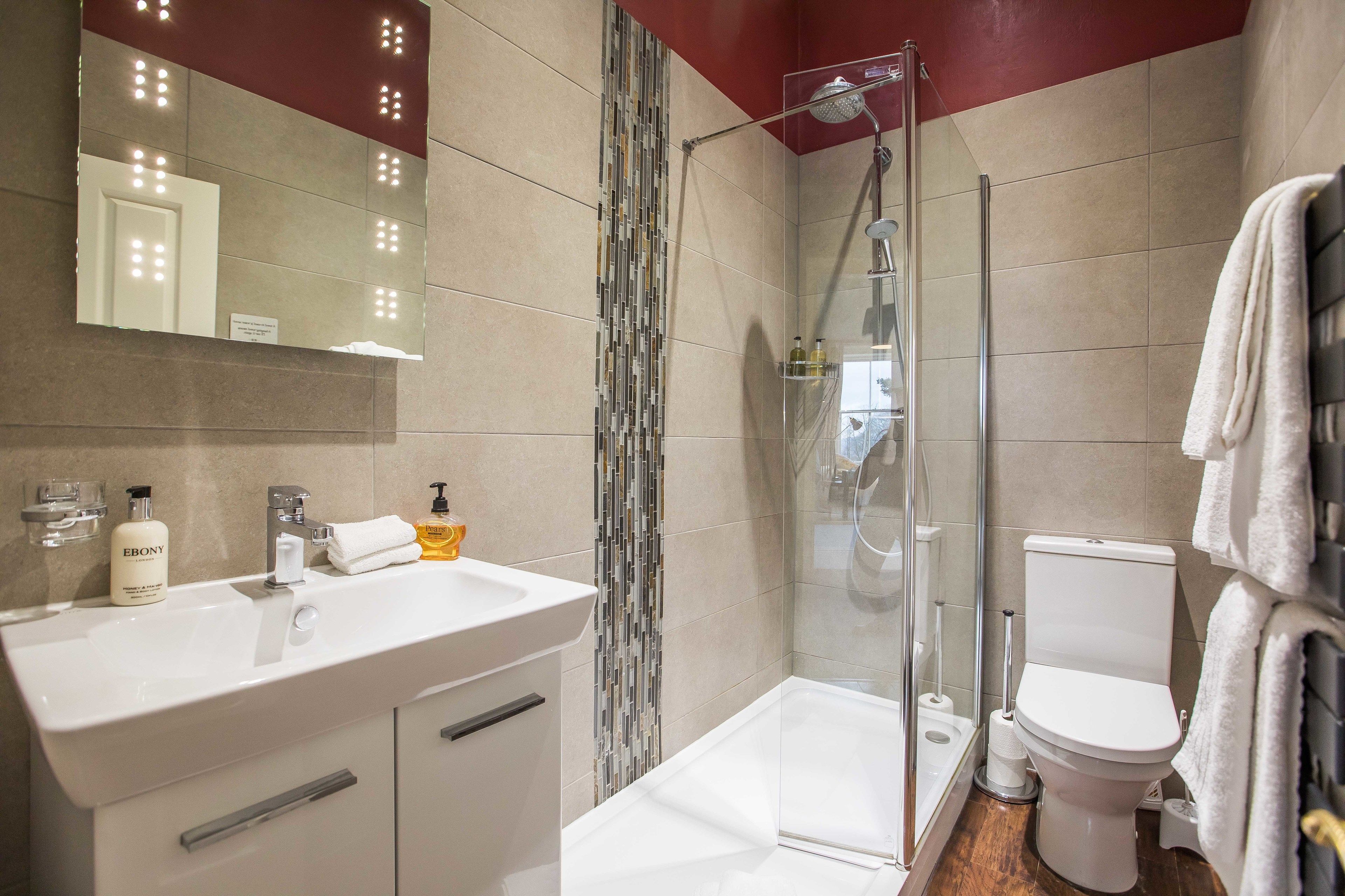 Un baño moderno con cabina de ducha de vidrio, un lavamanos blanco con espejo y un inodoro.