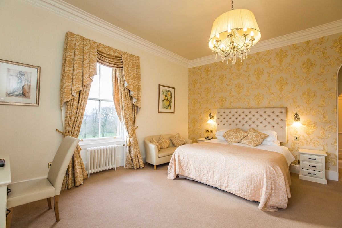 A bedroom with a large bed, a chair, a nightstand, and a window with curtains.