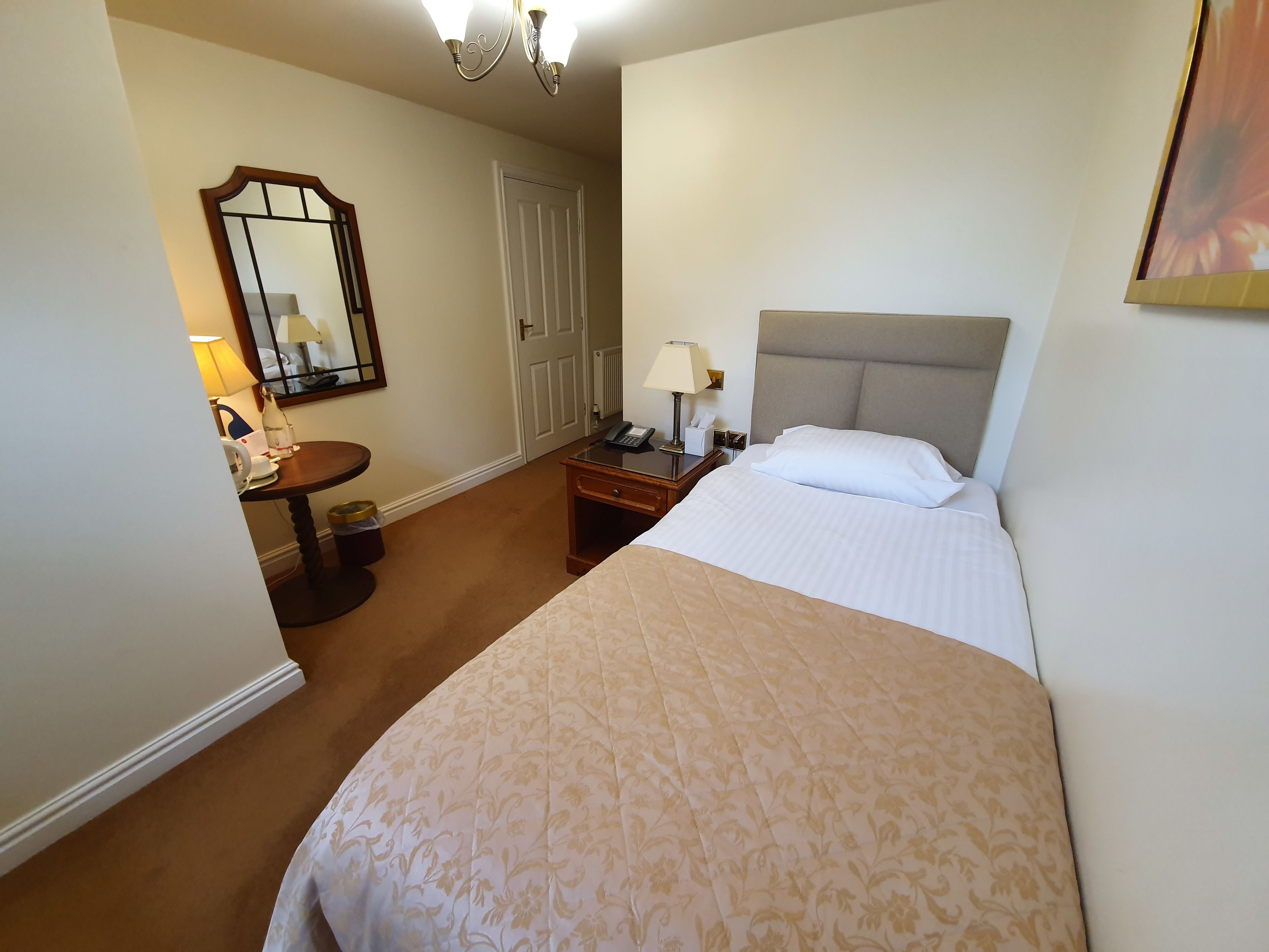 Una habitación de hotel con una cama grande, una mesita de noche con lámpara, un tocador y una puerta.