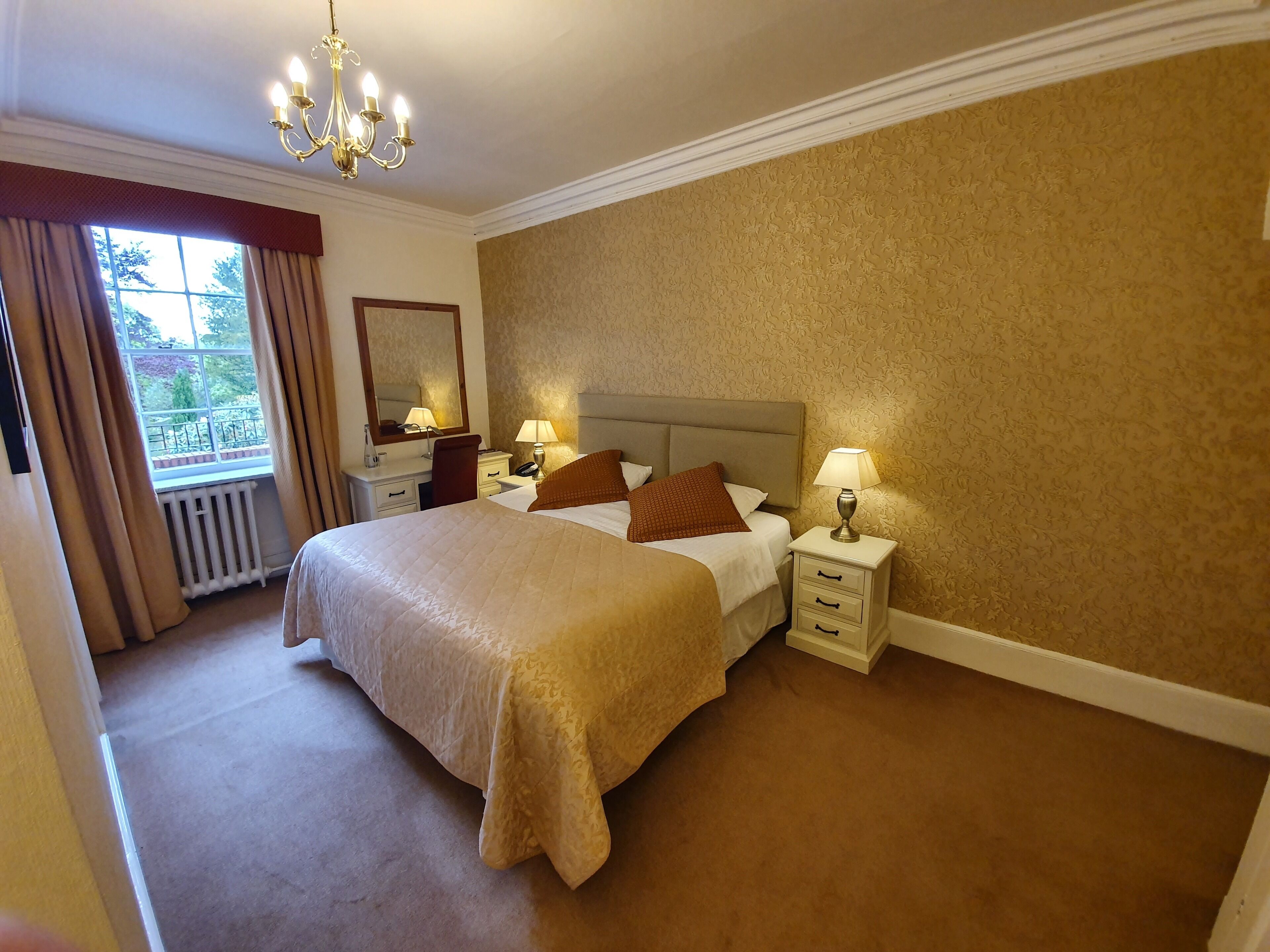 A hotel room with a large bed, two bedside tables with lamps, a dresser, a mirror, and a window with curtains.